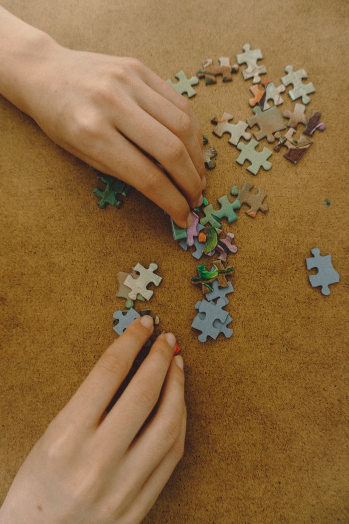 A close-up view of hands assembling colorful jigsaw puzzle pieces on a wooden surface.